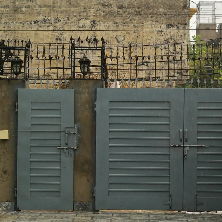 Portón metálico gris de dos hojas en el acceso de una casa